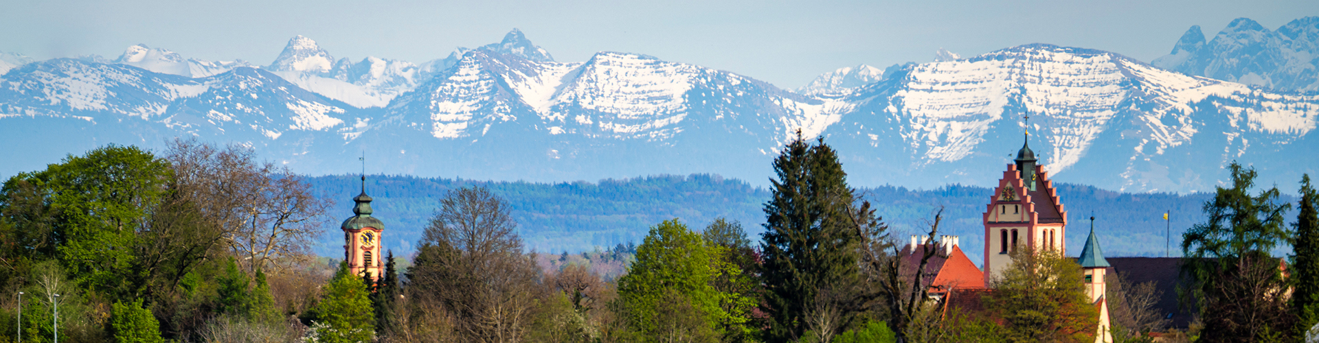 Blick auf die Alpen, vordergründig Kirchturmspitzen der Gemeinde Altshausen. Es herrscht klares Wetter.