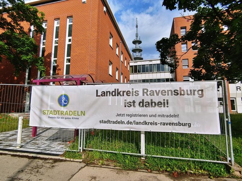 Vor einem Backsteinverwaltungsgebäude steht auf der Wiese davor ein Banner mit der Aufschrift Stadtradeln und Landkreis Ravensburg ist dabei.