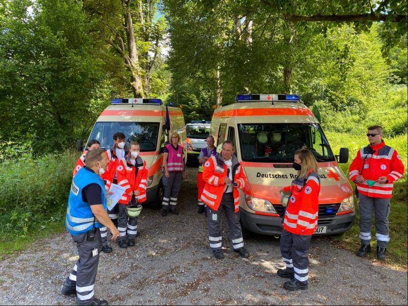 Menschen in Schutzkleidung stehen vor Rettungswagen. Im Hintergrund Bäume.