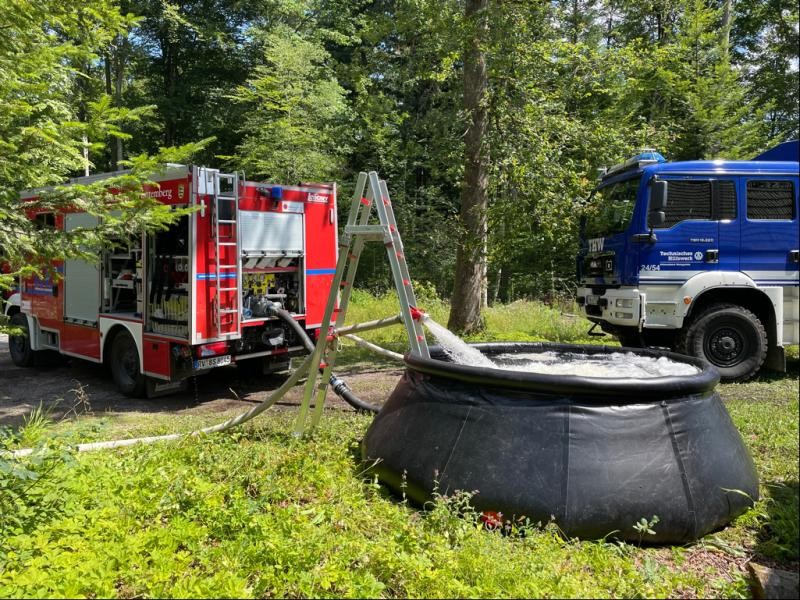 Ein Wasserbecken auf einer Lichtung. Daneben Rettungsfahrzeuge.