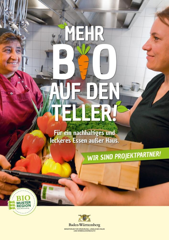 Werbeplakat, auf dem zwei Frauen abgebildet sind. Eine gibt der anderen eine Kiste mit Gemüse wie Paprika, Lauch und Salat. Sie befinden sich in einer Großküche. Auf dem Plakat steht geschrieben: Mehr Bio auf den Teller! Für ein nachhaltiges und leckeres Essen außer Haus.